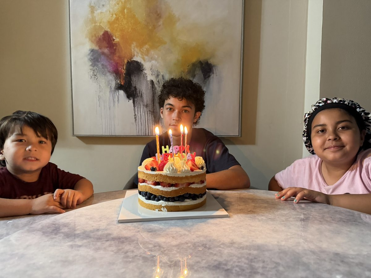 Theodore and his siblings around a birthday cake with lit candles
